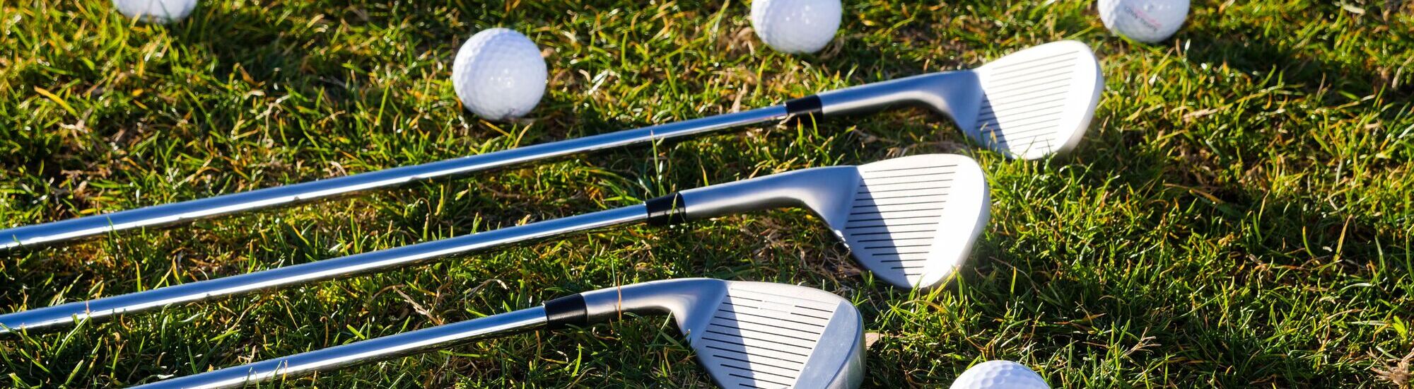 Three golf clubs resting on grass with several golf balls nearby, showcasing a golf practice setting.